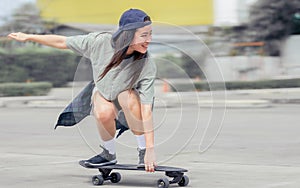 Beautiful happy Asian healthy woman smiling, motion speed riding and playing extreme sportive skateboard as outdoor activity with