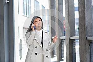 Beautiful and happy asian woman talking on the phone, chinese woman walking during a break near the office, business woman
