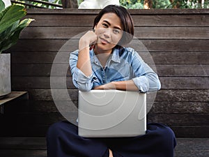 Beautiful happy asian woman wearing blue jeans shirt with laptop computer on her lap