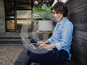 Beautiful happy asian woman wearing blue jeans shirt using laptop computer on her lap in cafe