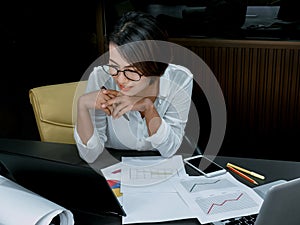 Beautiful happy Asian woman working overtime with laptop computer on desk in office