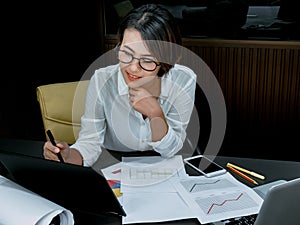 Beautiful happy Asian woman working overtime with laptop computer on desk in office