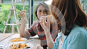 Beautiful happy Asian women lesbian lgbt couple sitting each side eating a plate of Italian seafood spaghetti and french fries.