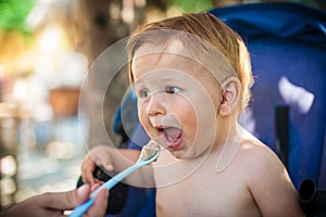 Beautiful happy baby boy eating porridge food, with a spoon