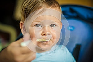 Beautiful happy baby boy eating porridge food, with a spoon