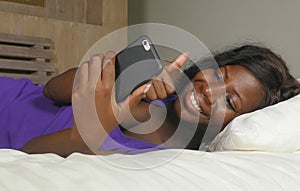 Beautiful and happy black African American woman lying relaxed on bed using internet mobile phone smiling cheerful networking
