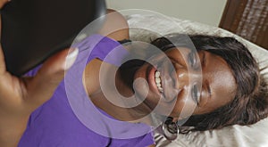 Beautiful and happy black African American woman lying relaxed on bed using internet mobile phone smiling cheerful networking
