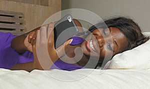 Beautiful and happy black Afro American woman lying relaxed on bed using internet mobile phone smiling cheerful networking social