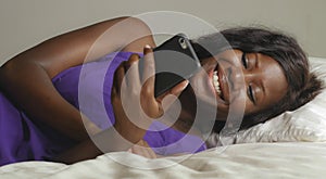 Beautiful and happy black Afro American woman lying relaxed on bed using internet mobile phone smiling cheerful networking social