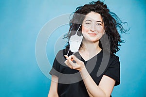 Beautiful happy black haired woman taking off medical antiviral mask.