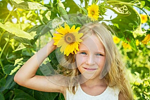 Beautiful happy blonde little girl on sunflower field. Girl holds flower in hand.