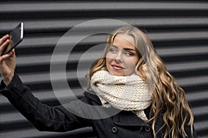 Beautiful happy blonde young Caucasian woman taking a selfie on smartphone outdoors in park in autumn