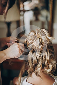 Beautiful happy bride getting her hair done by professional hair stylist in hotel room. Morning preparation before wedding