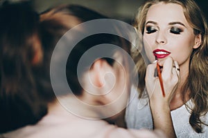 Beautiful happy bride getting her makeup done by professional make up artist in hotel room. Morning preparation before wedding