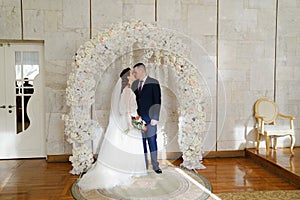 beautiful and happy bride and groom in an arch of flowers at wedding ceremony