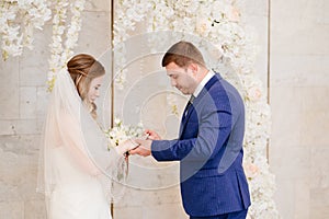 beautiful and happy bride and groom exchange rings in an arch of flowers