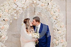 beautiful and happy bride and groom kiss in an arch of flowers