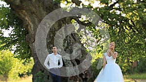 Beautiful happy bride and groom posing near the green tree in the forest
