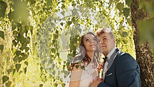 Beautiful and happy bride and groom under the branches of the birch trees rejoice together. Cheek to cheek with closed