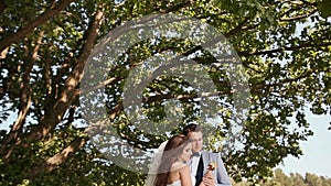 A beautiful and happy bride and groom under the branches of a tree together. Gentle touch of the hands. Kiss. I like