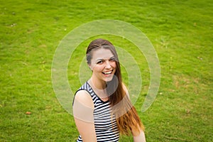 Beautiful happy brunette young woman smiling on green grass outside