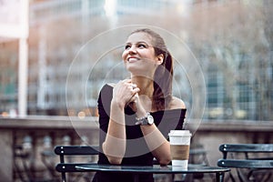 Beautiful happy businesswoman sitting in city park during lunch time or coffee break with paper coffee cup.