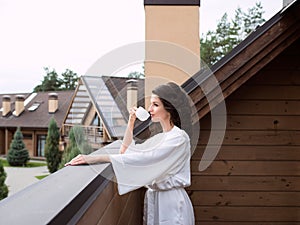 Beautiful happy cheerful brunette woman in white silk robe drinking coffee