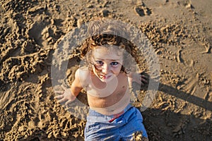 beautiful happy child sitting on the sand looking at the camera, close-up portrait