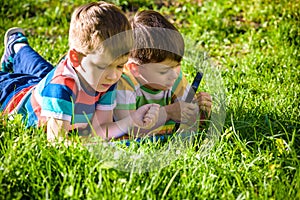 Beautiful happy children, boy brothers, exploring nature with magnifying glass, summertime