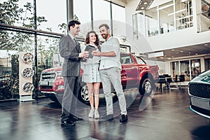 Beautiful happy couple buying a car at car salon showroom handsome car salesman showing something on a digital tablet to his