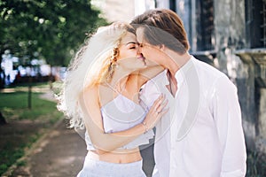 Beautiful happy couple in love walking and gently hugging in sunny green street. stylish hipster groom and blonde bride embracing