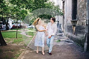 Beautiful happy couple in love walking and gently hugging in sunny green street. stylish hipster groom and blonde bride embracing