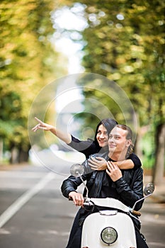 Beautiful happy couple riding scooter and having fun, woman pointed with hands and smiling.