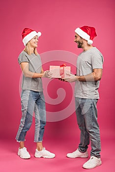 beautiful happy couple in santa hats gifting christmas present