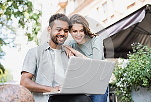 Beautiful happy couple using laptop. Joyful smiling woman and man looking at computer in city in summer.