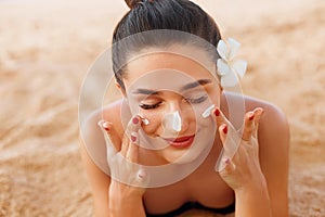 Beautiful happy cute woman applying suntan cream to her nose on the beach. Body Sun protection. Sunscreen. photo