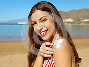 Beautiful happy cute woman applying suntan cream to her nose and shoulder with beach background