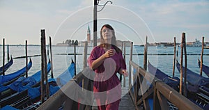 Beautiful happy dark haired young Caucasian tourist woman walks to camera on famous gondola pier in sunrise Venice Italy