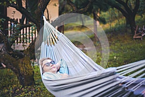 Beautiful happy elderly woman relaxing in a hammock in the garden of a country house. Happy retirement lifestyle
