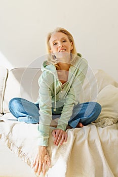 Beautiful happy elderly woman smiling at camera while relaxing on sofa at home