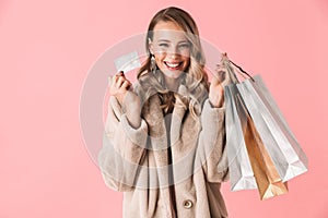 Beautiful happy excited young pretty woman posing isolated over pink wall background holding shopping bags and credit card