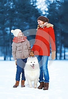Beautiful happy family having fun, mother and son walking with white Samoyed dog outdoors in winter day