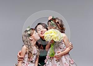 Beautiful happy family mom and two little cute girls in wreaths of fresh flowers and a large bouquet of tulips kiss, laugh and hug