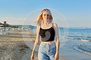 Beautiful happy female teenager 16 years old walking along sea sandy beach, at sunset