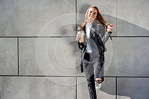 Beautiful happy girl with cold fresh smoothie outdoors. Smiling hipster girl with cup of milkshake on city street.