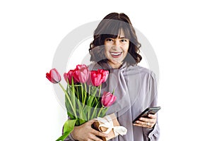 Beautiful happy girl holding red tulips, gift box and phone on white background indoors, space for text. Stylish young woman