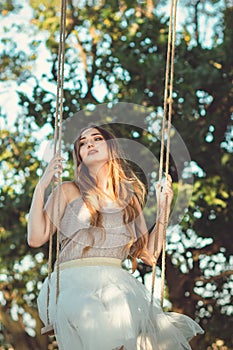 Beautiful happy girl with long hair swinging on rope swing on summer nature, young woman enjoy flying in foliage, leisure activity