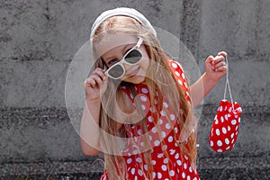 Beautiful happy girl in a red polka dot dress smiling on on concrete wall background. Cute joyful child with long hair