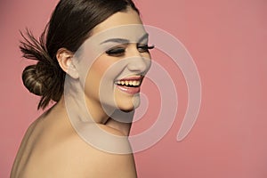 A beautiful happy girl with smooth skin and make-up on a pink background. The hairs are gathered in a bun at the back of the head