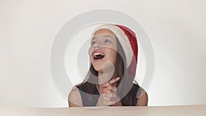 Beautiful happy girl teenager in a Santa Claus hat look and emotionally expresses a surprise on white background